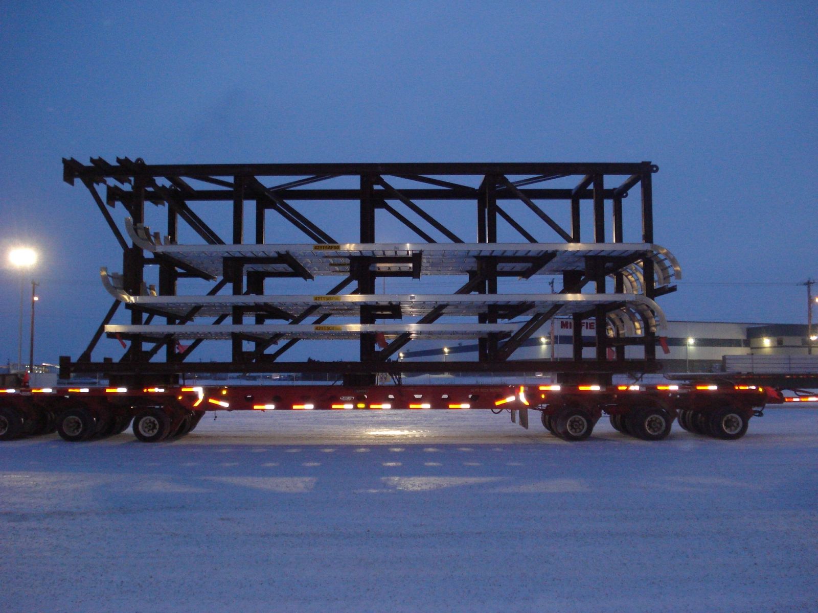 Large black metal framework loaded on a flatbed trailer at dusk.