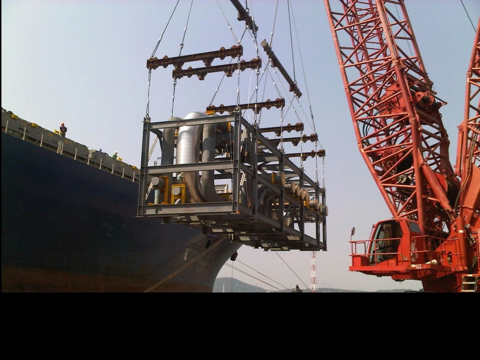 A crane lifts industrial equipment near a ship dock.