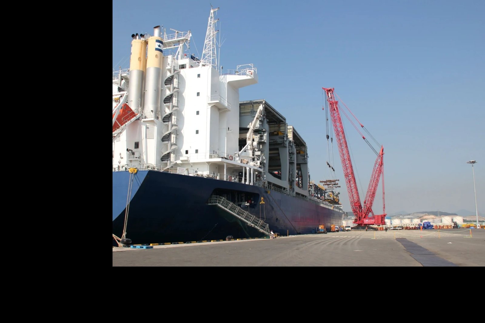 Large cargo ship docked at port with a red crane nearby.